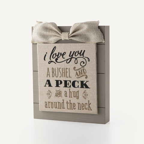 Wood sign with fabric bow, says "I love you a bushel and a peck and a hug around the neck."